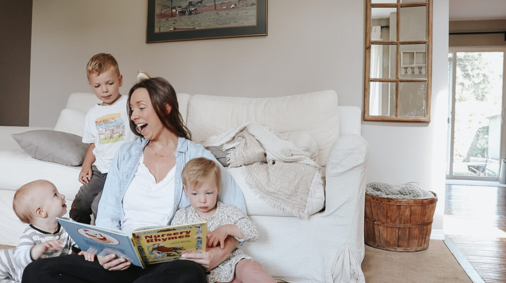 Christian homemaker reads book to her young children sitting on the floor in her living room